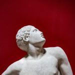 Grecian male statue looks up on red background