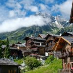 brown wooden houses near green trees and mountain under white clouds during daytime